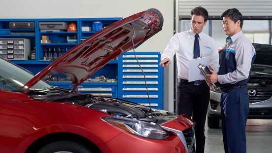 Image of a man in a tie and a mechanic standing next to a car with an open hood.