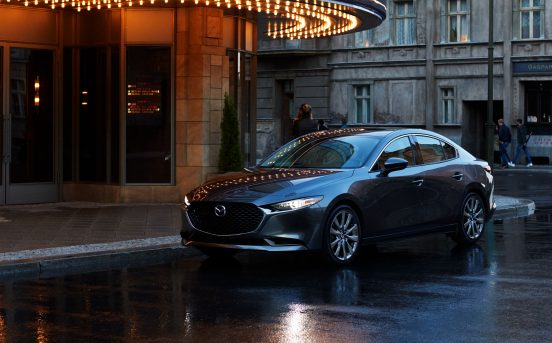 Image of a dark 2019 Mazda3 sedan parked outside of a theater.