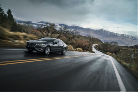 Image of a gray 2019 Mazda6 driving on a country highway in cloudy weather.