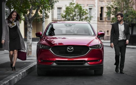 Image of a young couple walking by a red Mazda vehicle.