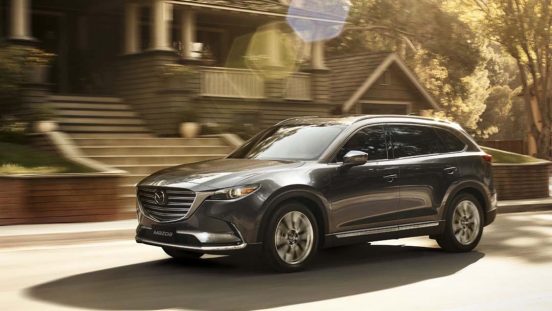 Image of a silver 2019 Mazda CX-9 driving on a suburban street.